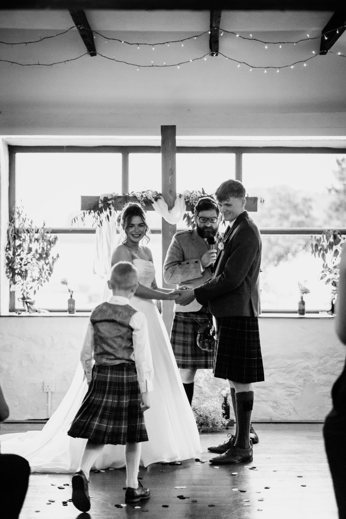 A young guest in a kilt walks past as Ellie and Nathan hold hands at the front