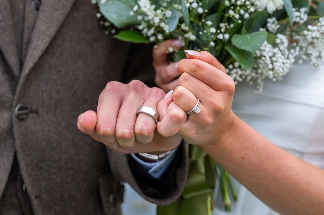 The couple show their wedding rings above the bouquet