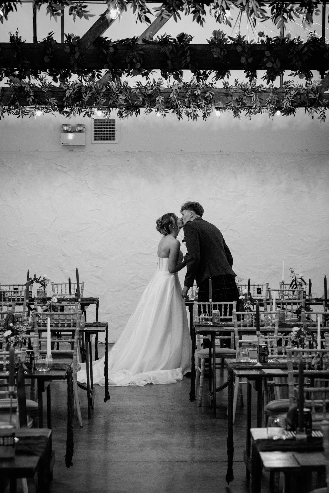 The couple share a kiss alone in the barn among the set tables