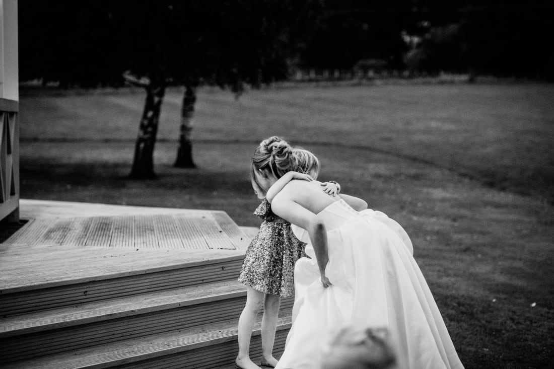 The bride bends down to hug a young guest on the decking steps