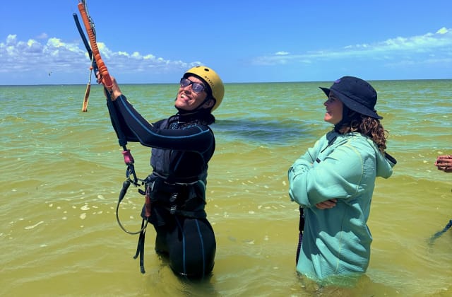 Student smiling in the water with kite, instructor next to them