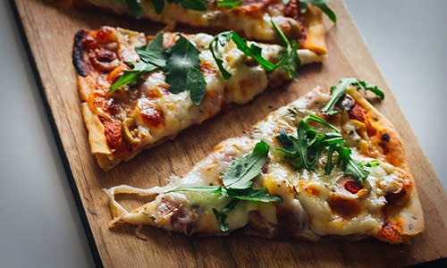 Changing to a vegetarian or vegan diet is an easy, effective climate change action. Image shows vegetarian pizza with cheese tomato jalapeno peppers and rocket on a wooden board