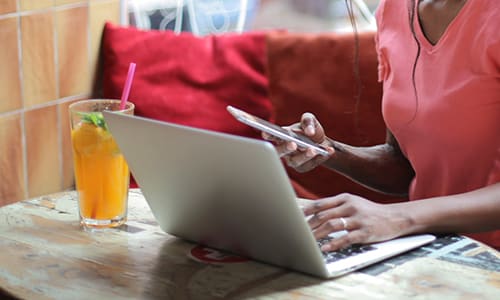 Climate change action - influence politicians, companies and other people. Image shows a casually dressed woman wearing pink using laptop and phone in a cafe with a warm colour scheme