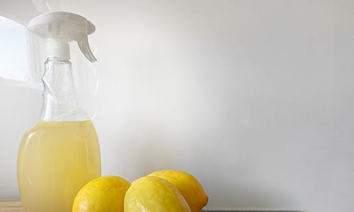 Climate change action - reduce harmful chemical use. Image shows a bottle of a natural cleaning product made of lemon juice and three lemons against a white background