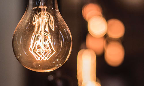 Climate change action - reduce energy. Image shows a powered-on incandescent light bulb, selective focus, with bokeh. Image is warm orange and brown in tone