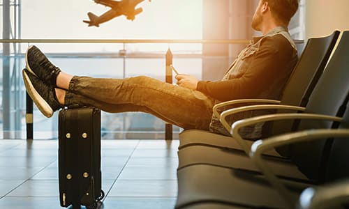 High impact climate change action. Image shows a man in airport departure lounge looking at plane taking off