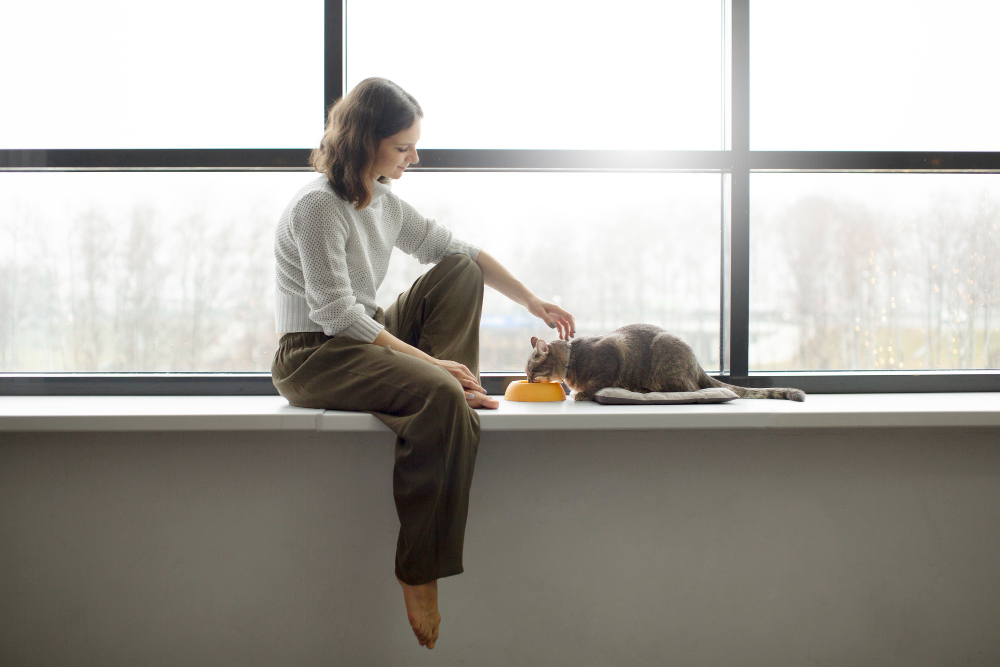 Jeune femme qui caresse sont chat pendant qu’il mange