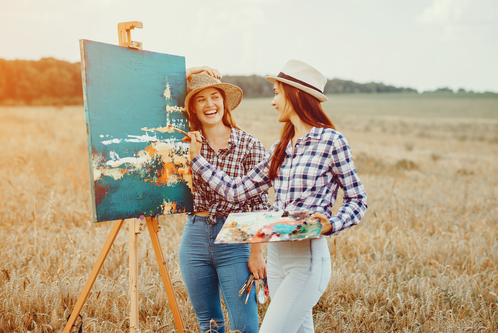 deux femmes qui sourient et rient dans la nature en faisant de la peinture sur toile