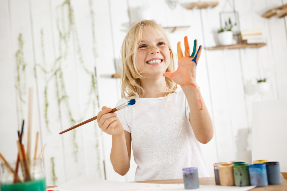 Petite fille qui souris fièrement et qui a de la peinture sur les mains
