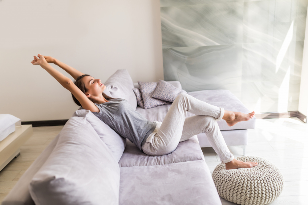 femme qui s’étire et se détend sur le canapé de son salon