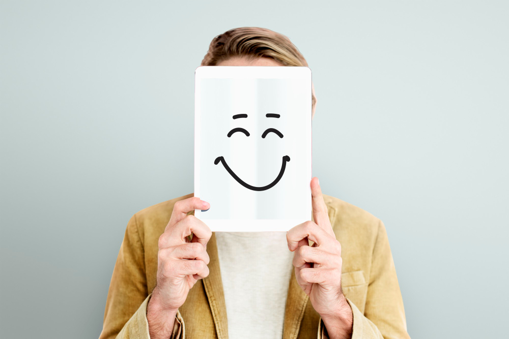 homme qui tient un papier devant son visage avec un smiley qui sourit dessiné dessus