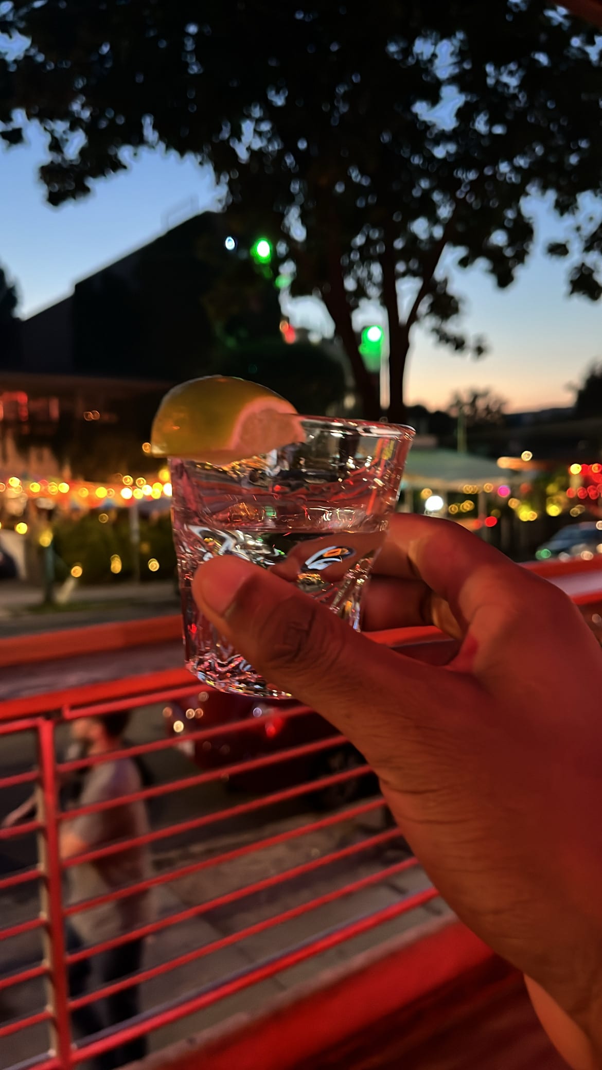 A hand raising a tequila shot with a lime wedge against the dusk, patio string lights behind