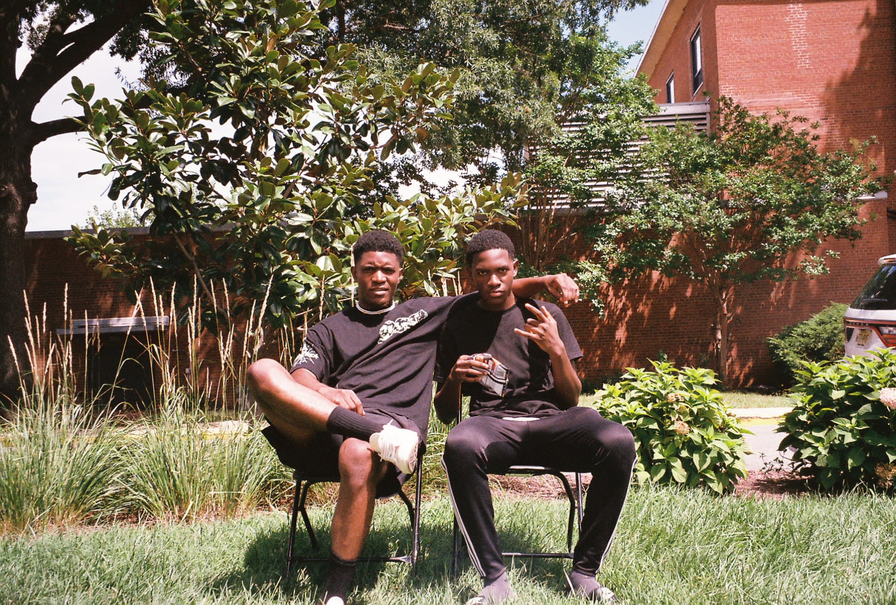 Shot on film: two friends in black tees posing on folding chairs in a sunlit garden