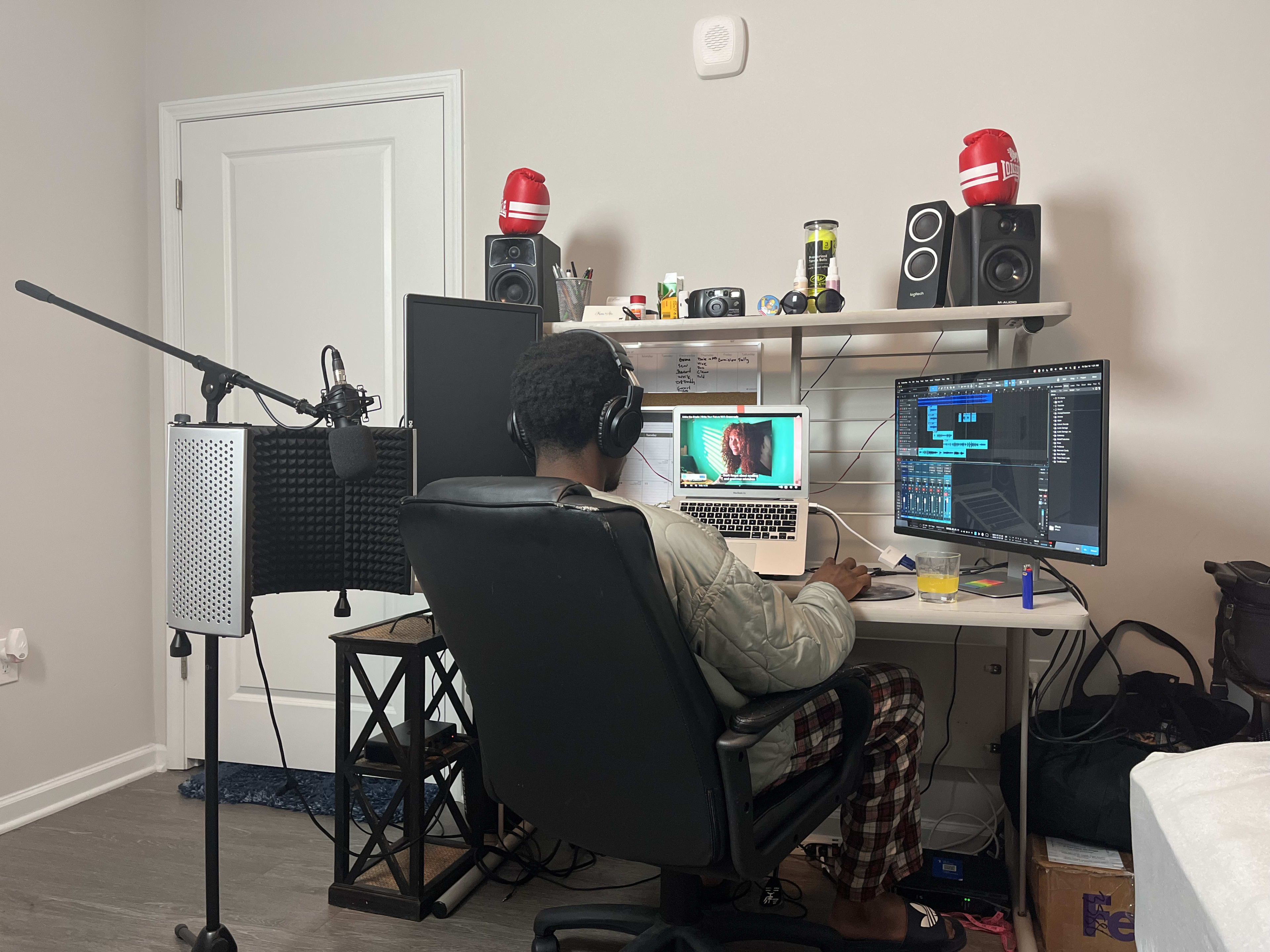 Kama in headphones working at his bedroom studio desk, mic and reflection filter at the ready