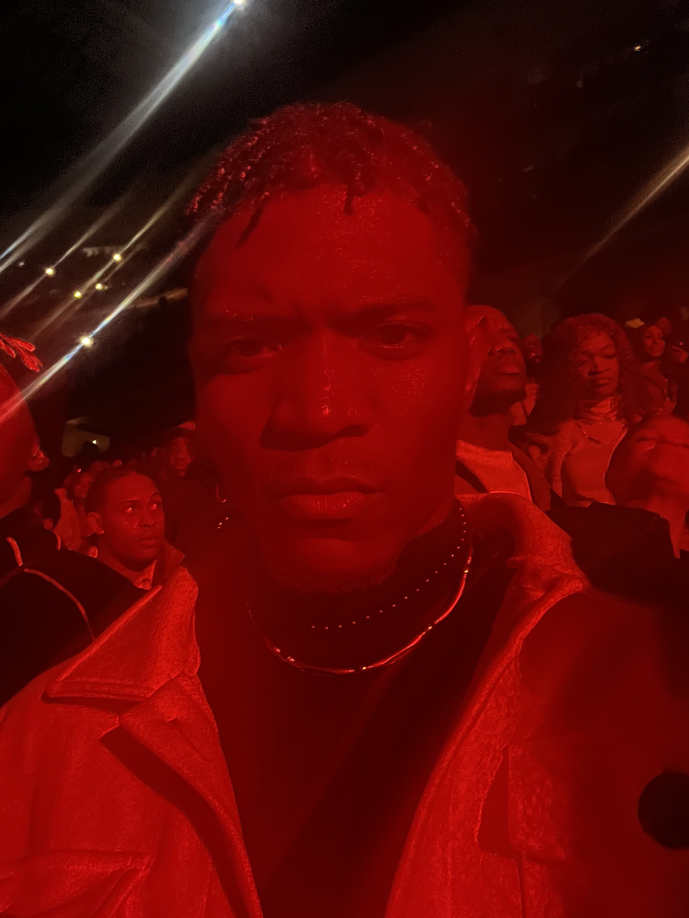 Selfie in a packed crowd washed entirely in red light, chains doubled at the collar