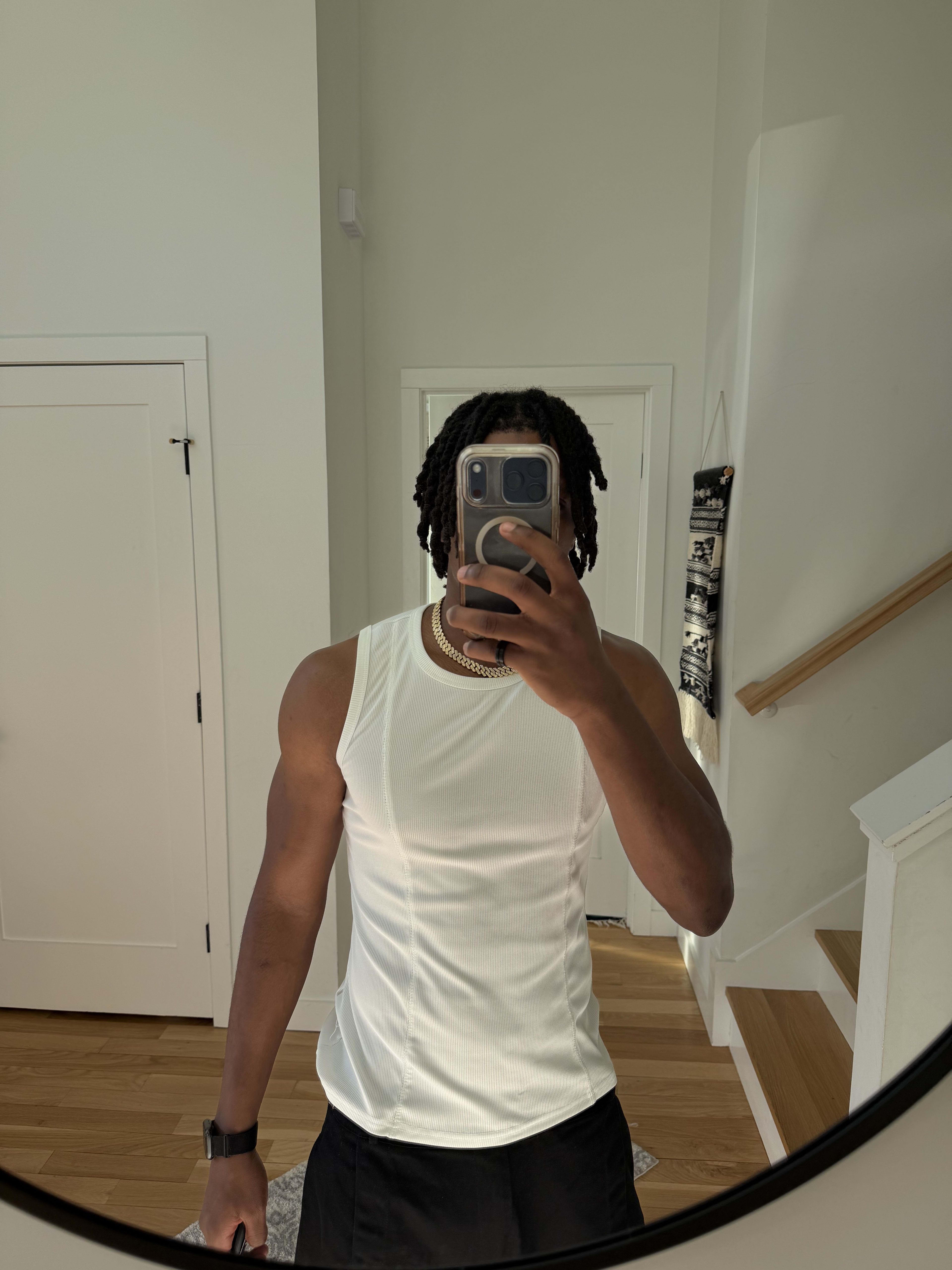 Mirror selfie in a white tank and silver chain by the staircase, twists down