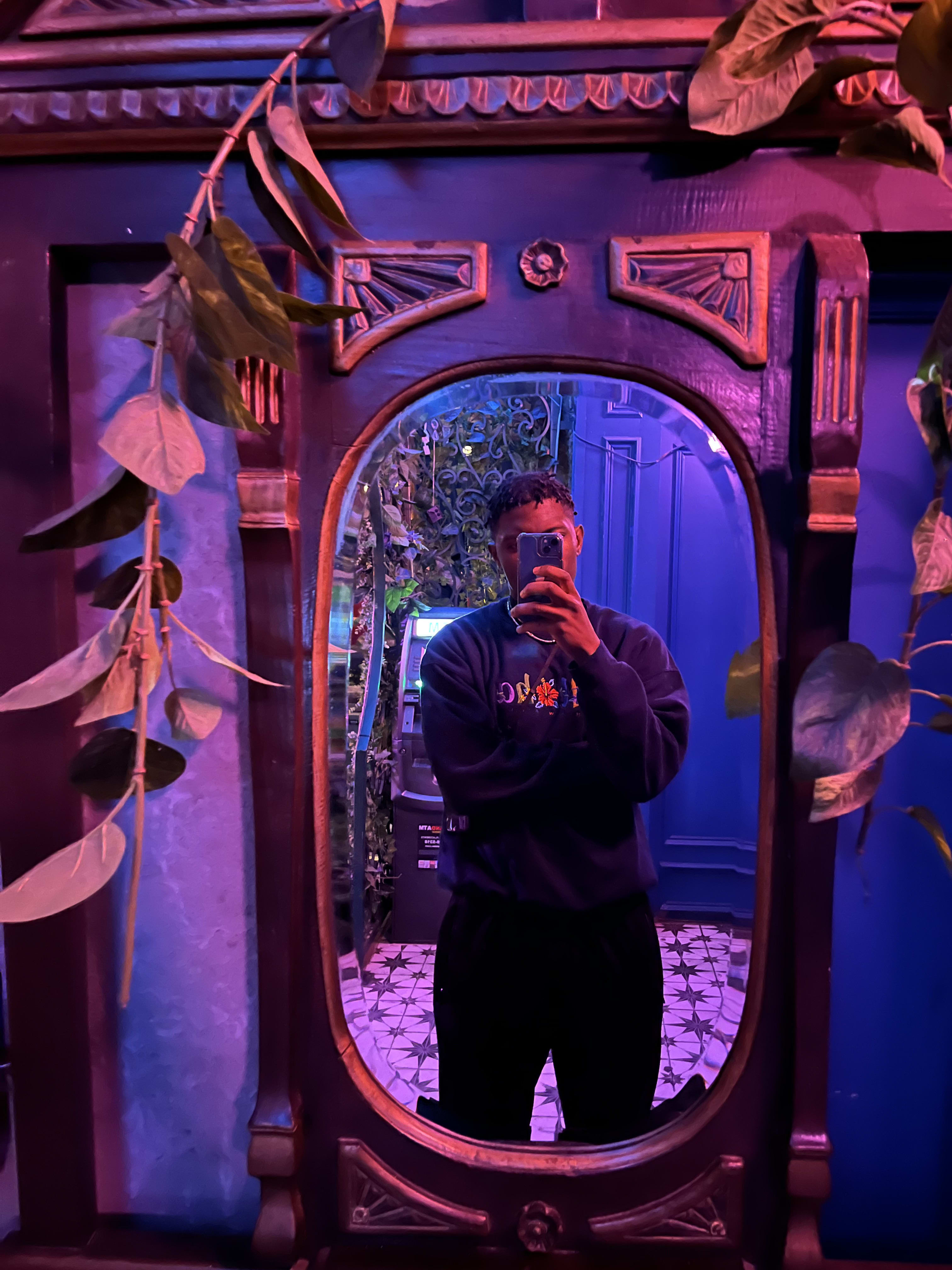 Mirror selfie in an ornate carved-wood mirror under purple light, embroidered sweatshirt on
