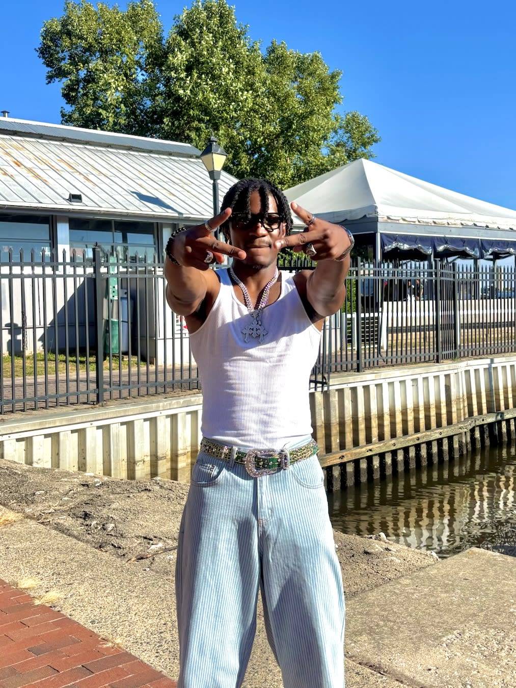 Kama at the waterfront in a white tank and striped jeans, rhinestone western belt, hands throwing signs