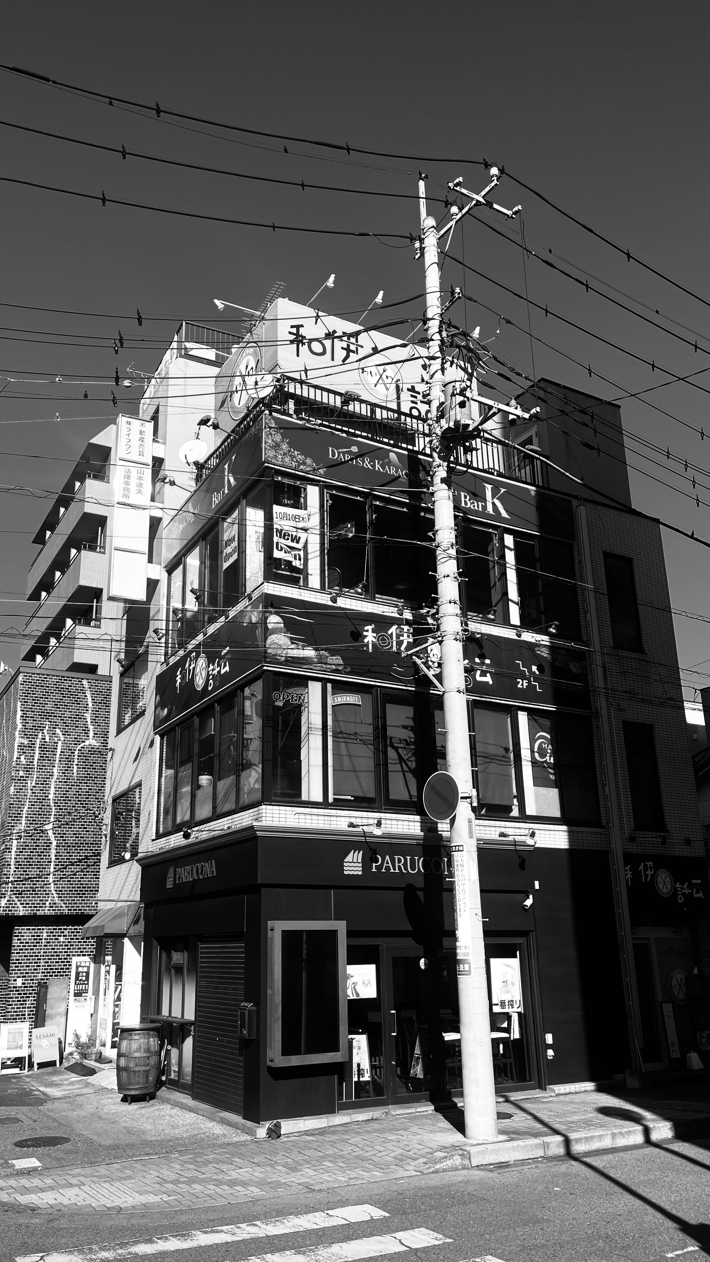 Black-and-white corner building strung with power lines - a darts and karaoke bar in Japan