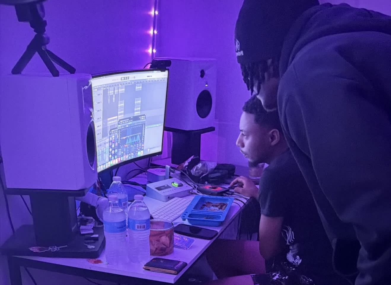 Purple-lit studio - the engineer dialing in the mix on a curved monitor, a friend leaning in