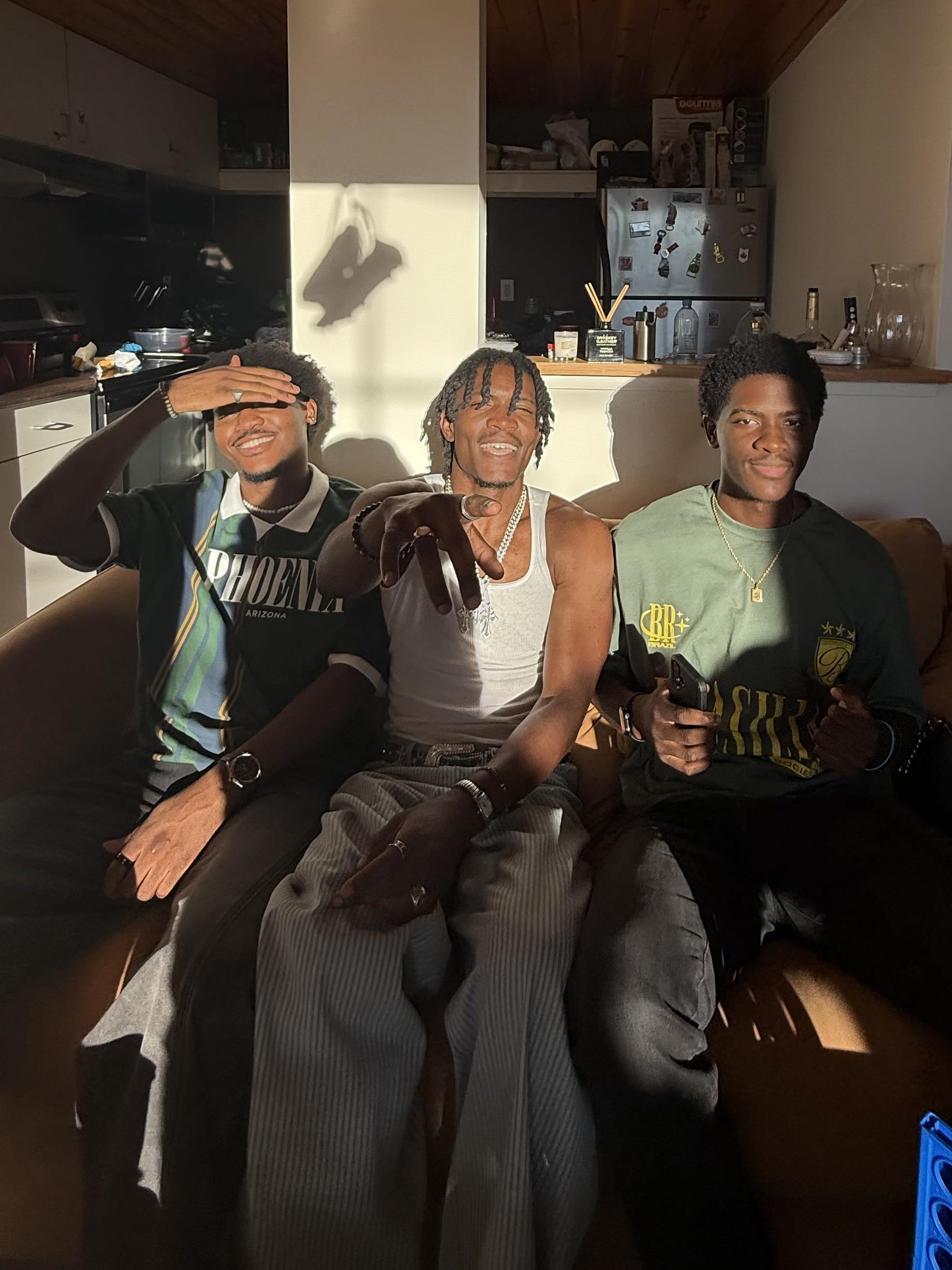 Three friends on the couch in golden light, Kama center in a white tank throwing a sign