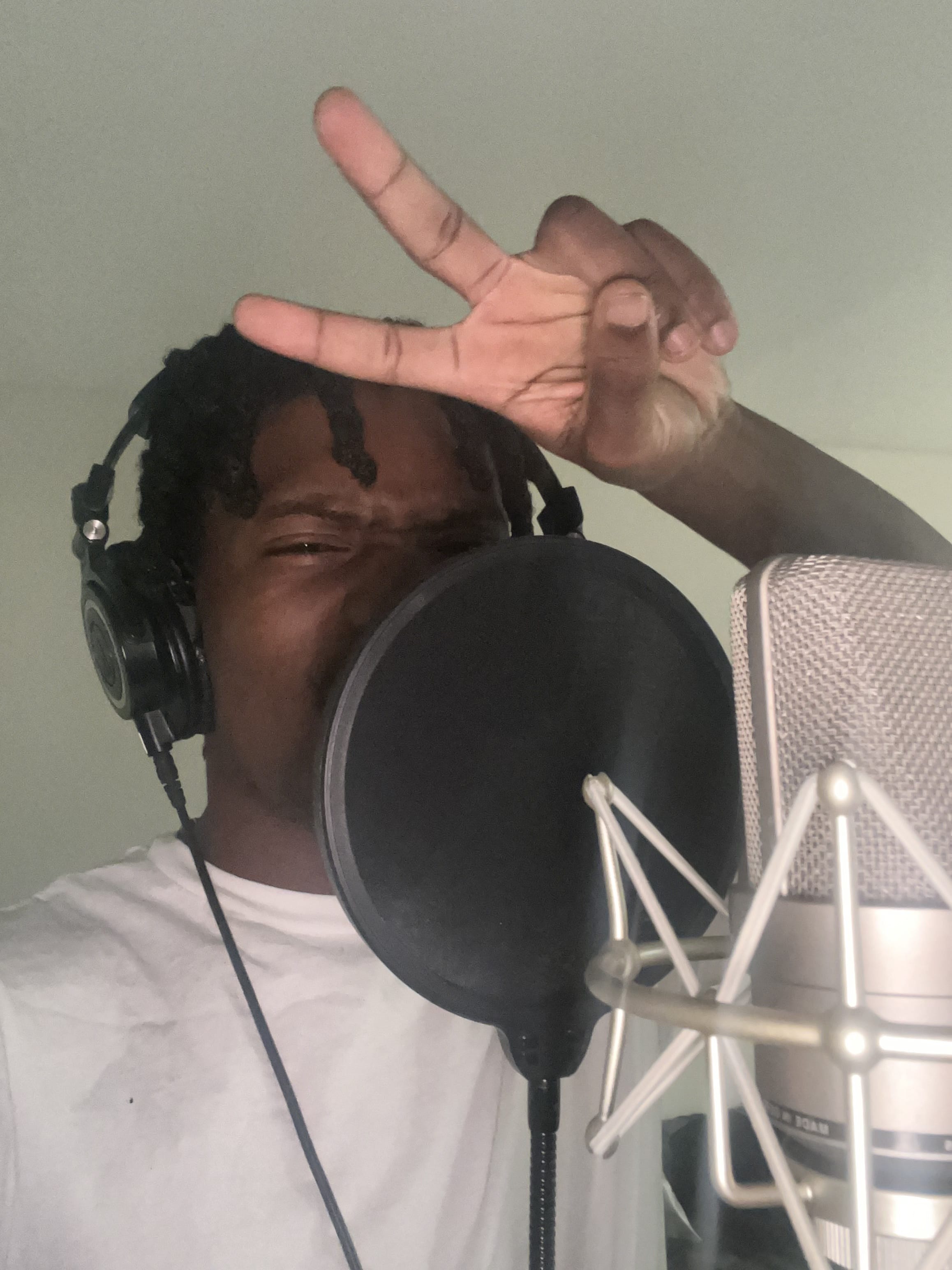 Selfie mid-take: headphones on, pop filter and condenser mic up, peace sign to the camera