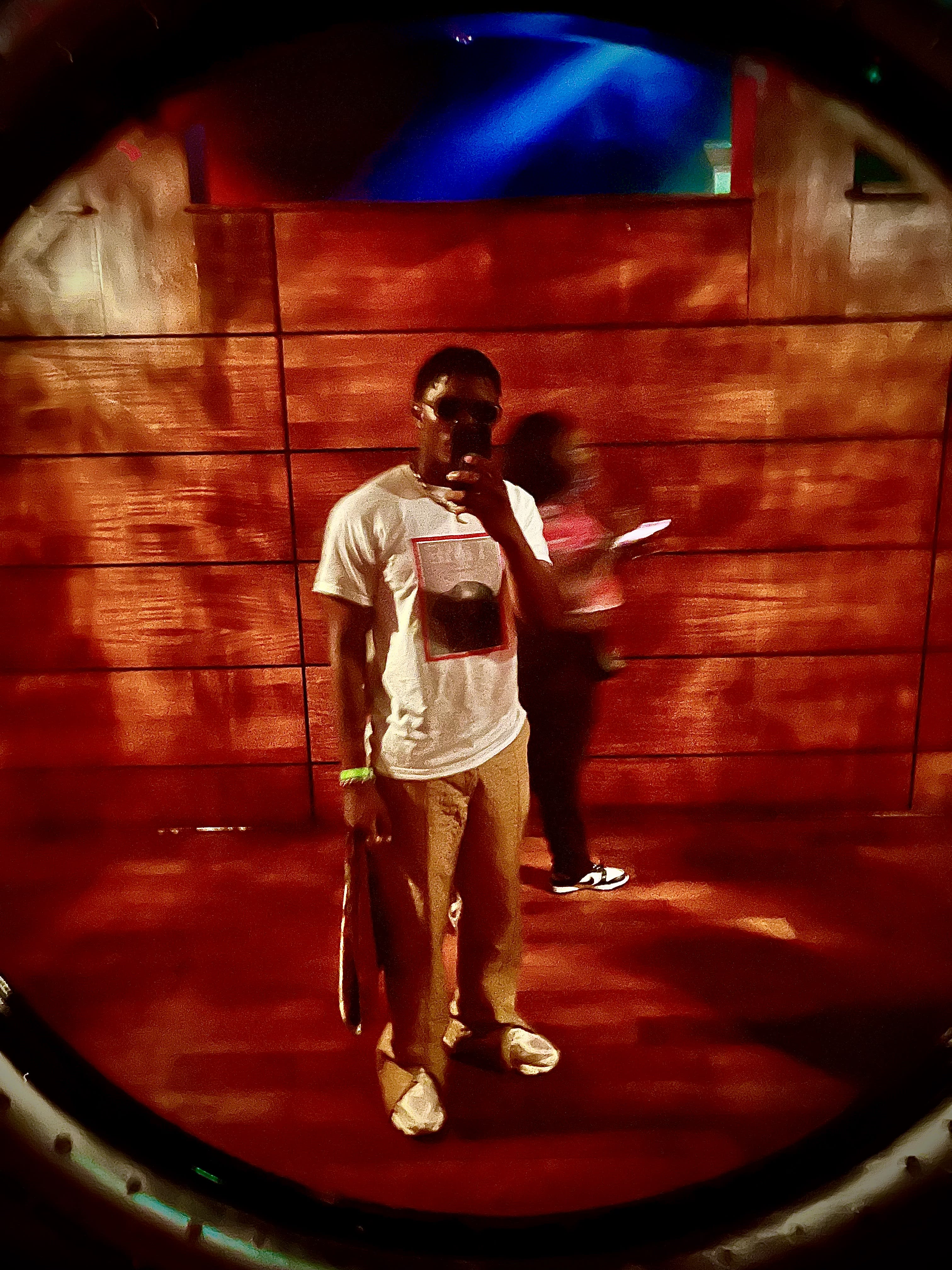 Through a porthole: Kama on a wood-paneled stage, mic up, blue light pouring from above