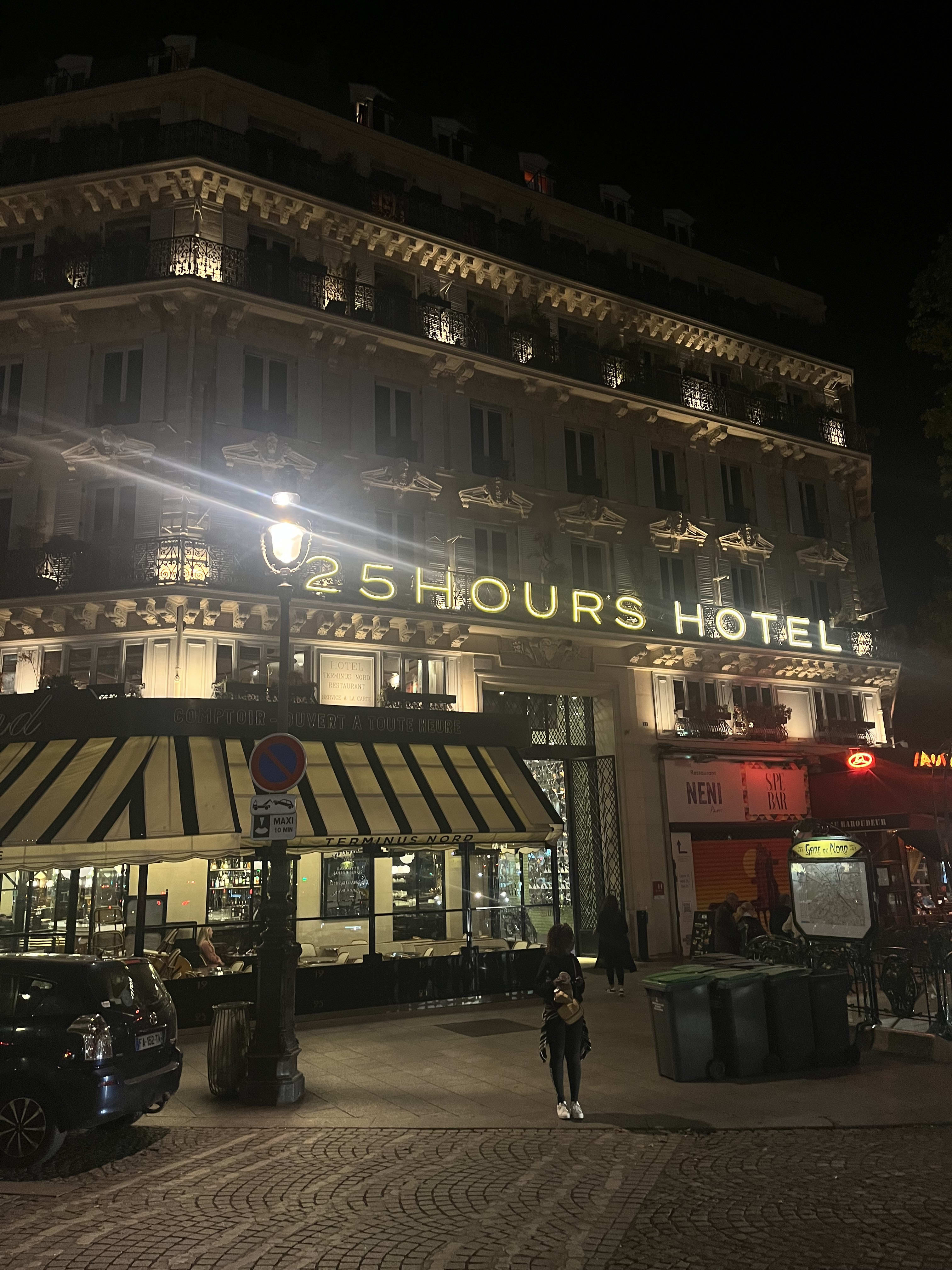 Paris at night - the 25hours Hotel facade lit gold above a striped cafe awning