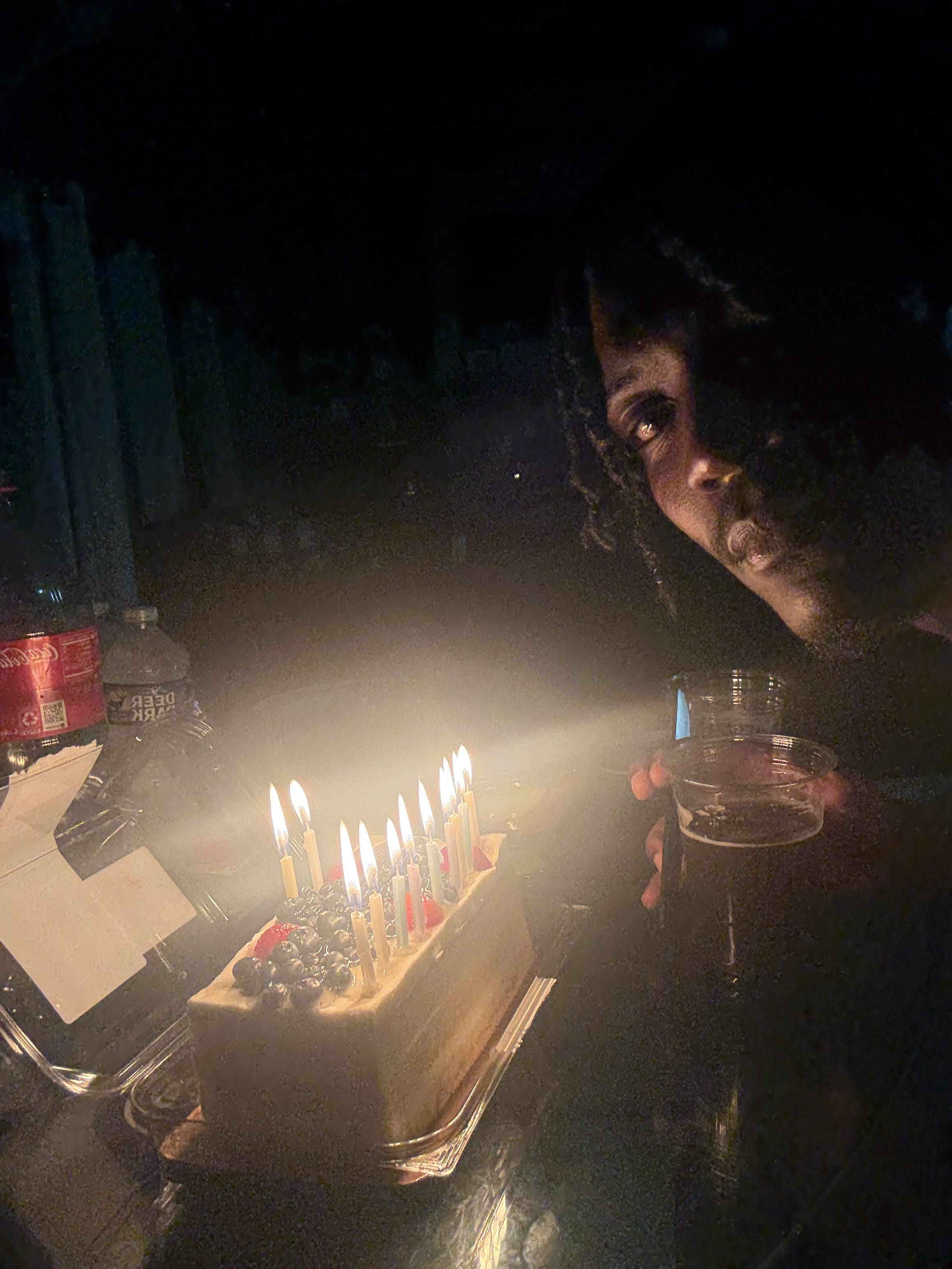 Birthday in the dark - candles blazing on the cake, drink in hand, face lit by the flames