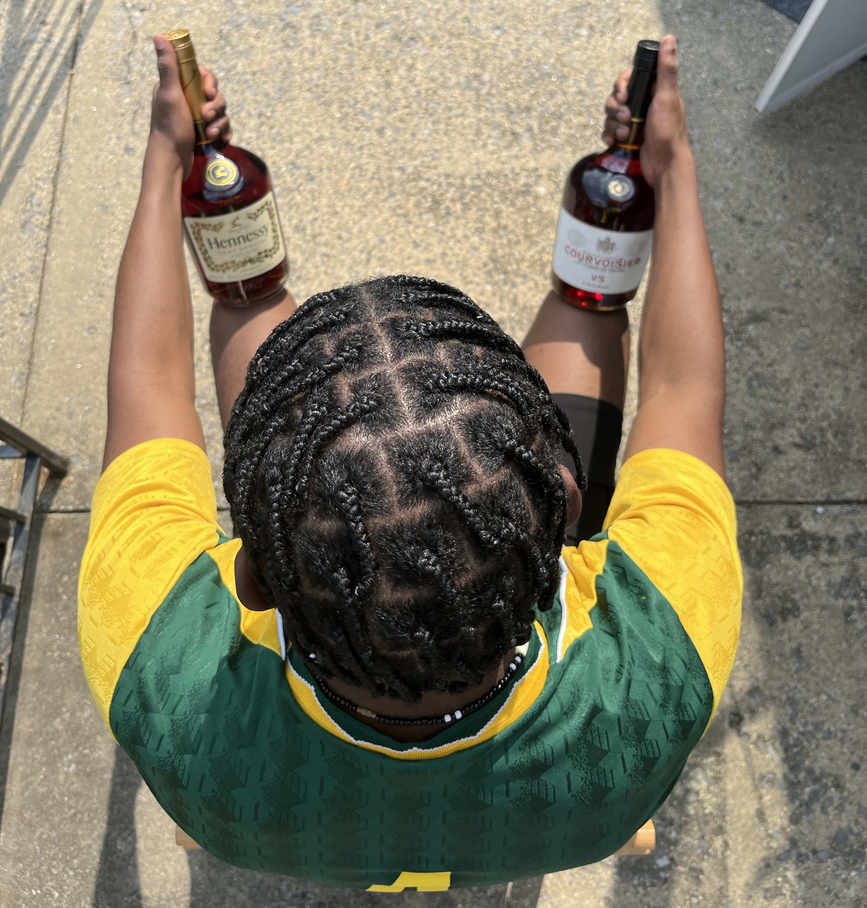 From above: braids fresh, green-and-yellow jersey, a bottle of cognac in each hand on the steps