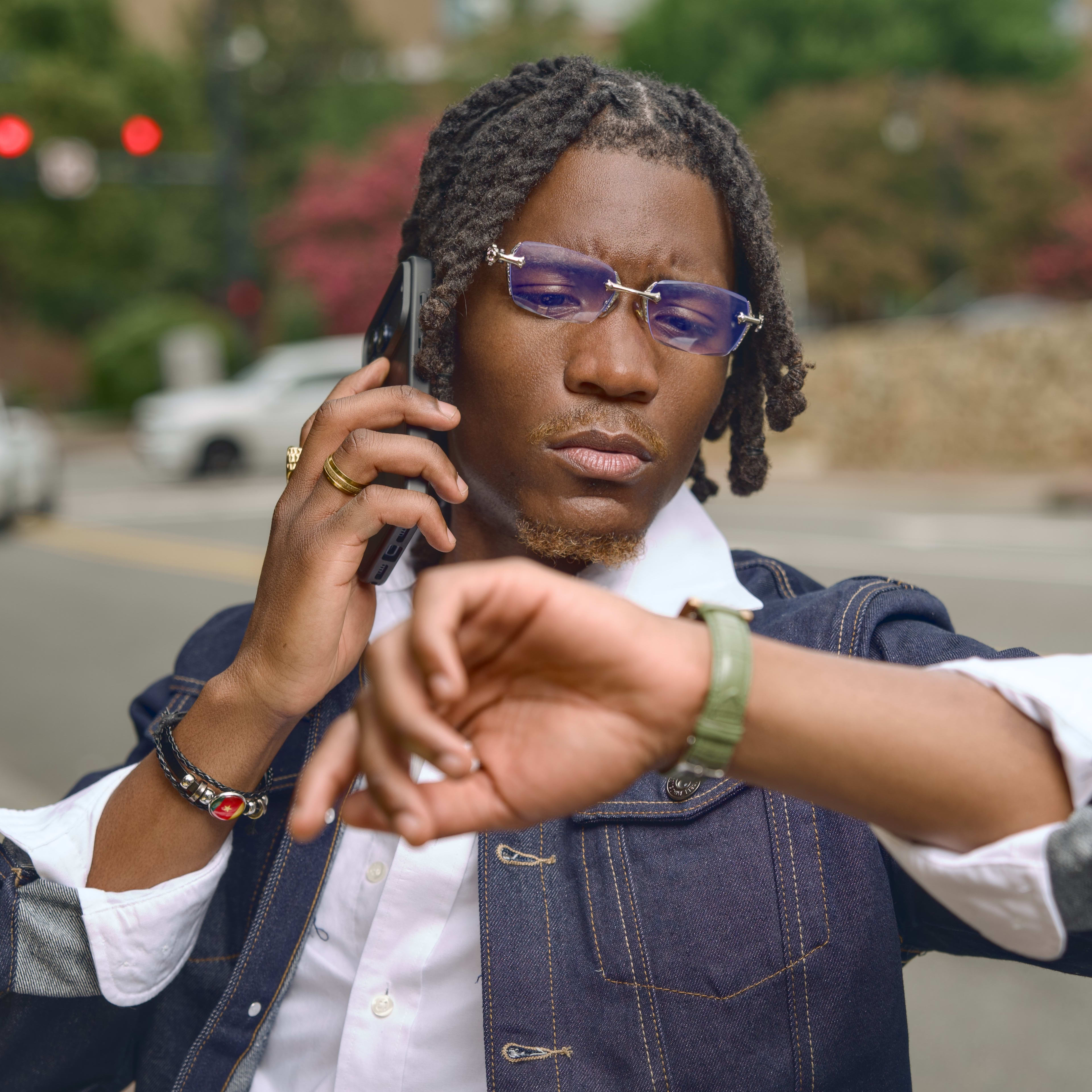 Phone to one ear, eyes on the watch - Kama in denim and rimless tints at the crosswalk