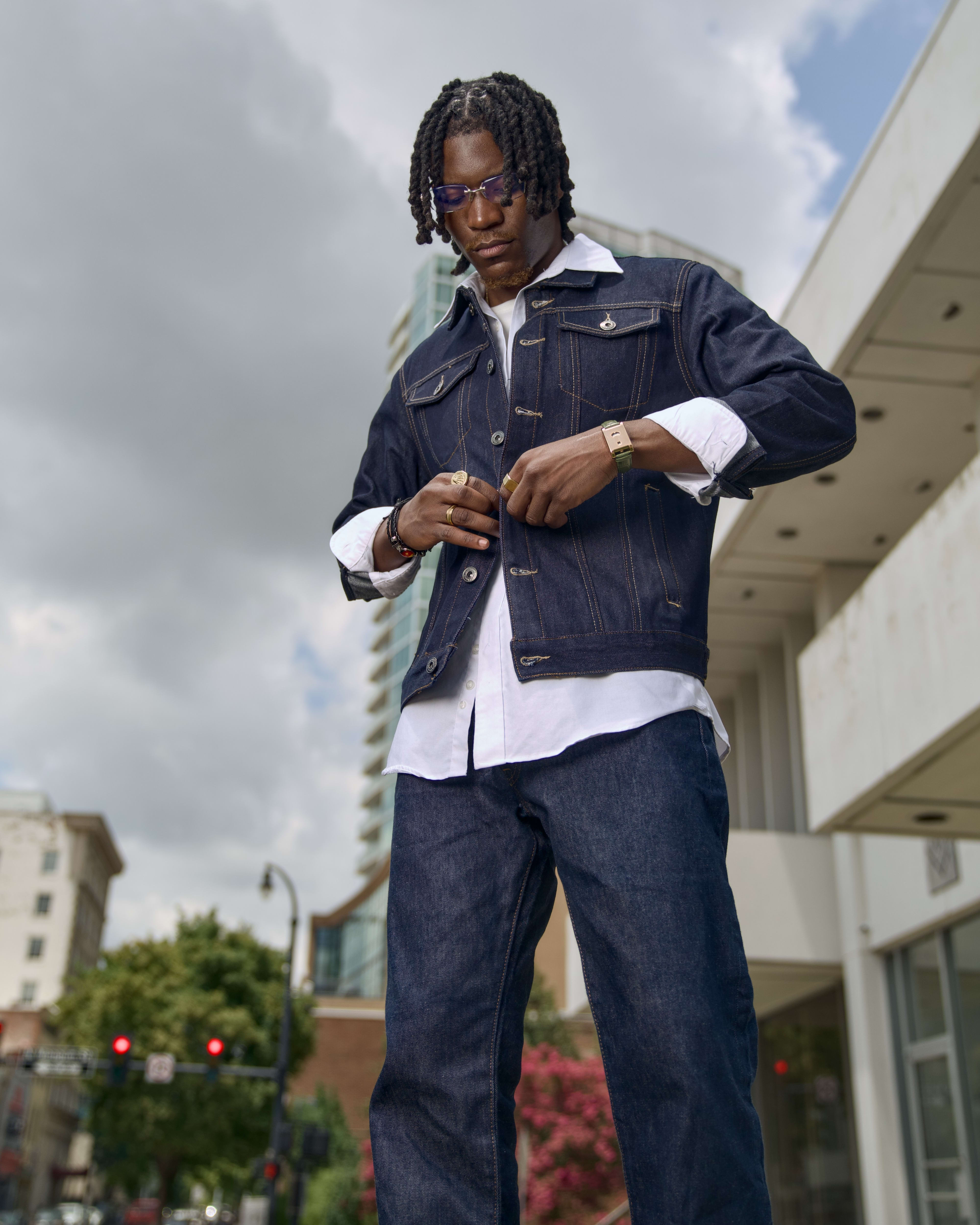 Low angle: Kama buttoning the denim jacket, storm clouds and towers behind