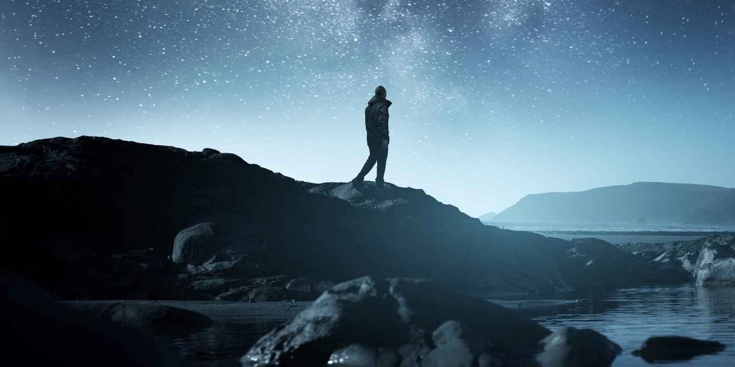 Calm Midnight adventures. A long exposure shot of a man staring up into the night sky, silhouetted against the milky way galaxy. Photo composite.