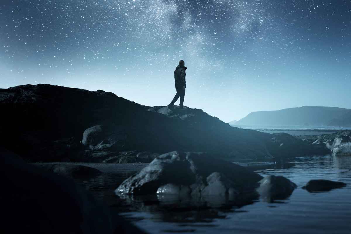 Calm Midnight adventures. A long exposure shot of a man staring up into the night sky, silhouetted against the milky way galaxy. Photo composite.