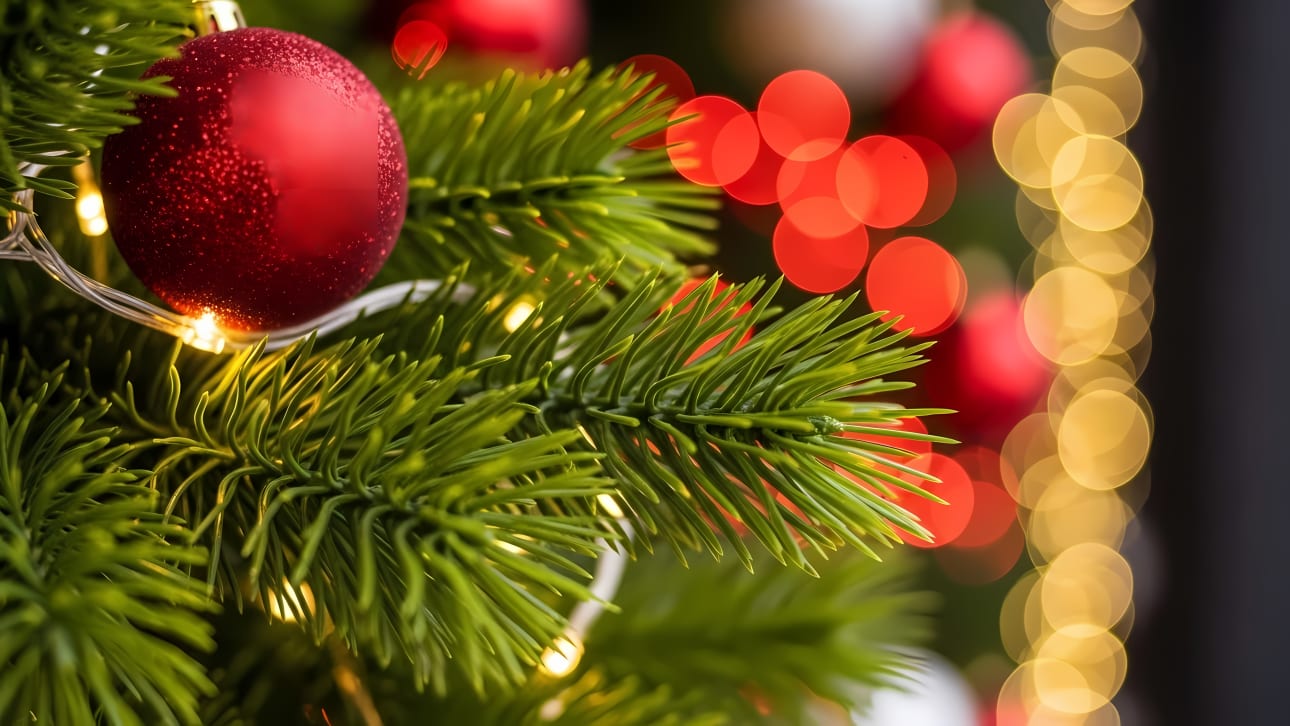 Close-up of a festive Christmas tree branch adorned with a red glittery ornament and sparkling bokeh lights, perfect for holiday designs.