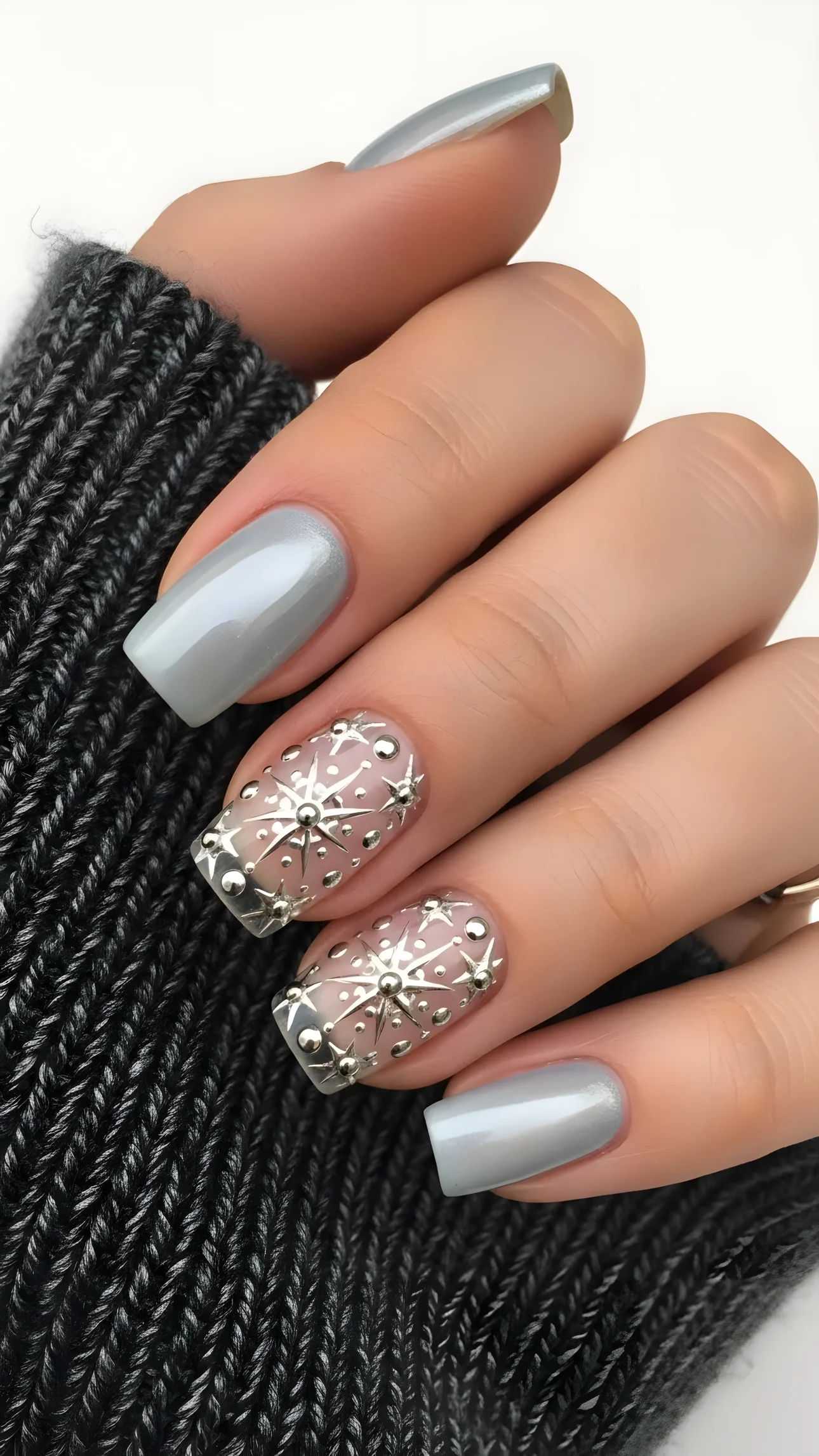 Woman's hand displays silver nail art with star designs against a dark gray knitted sweater background.