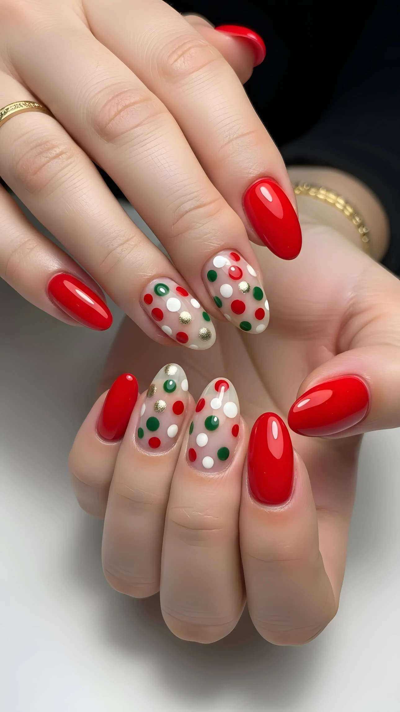 Close-up of hands with red and polka dot holiday manicure featuring red, green, and gold dots on a clear base.