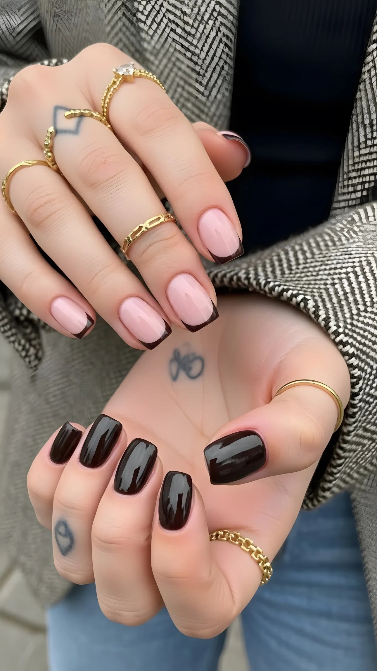 Woman's hands with dark and French tip manicures, adorned with gold rings, showcasing modern beauty aesthetic.
