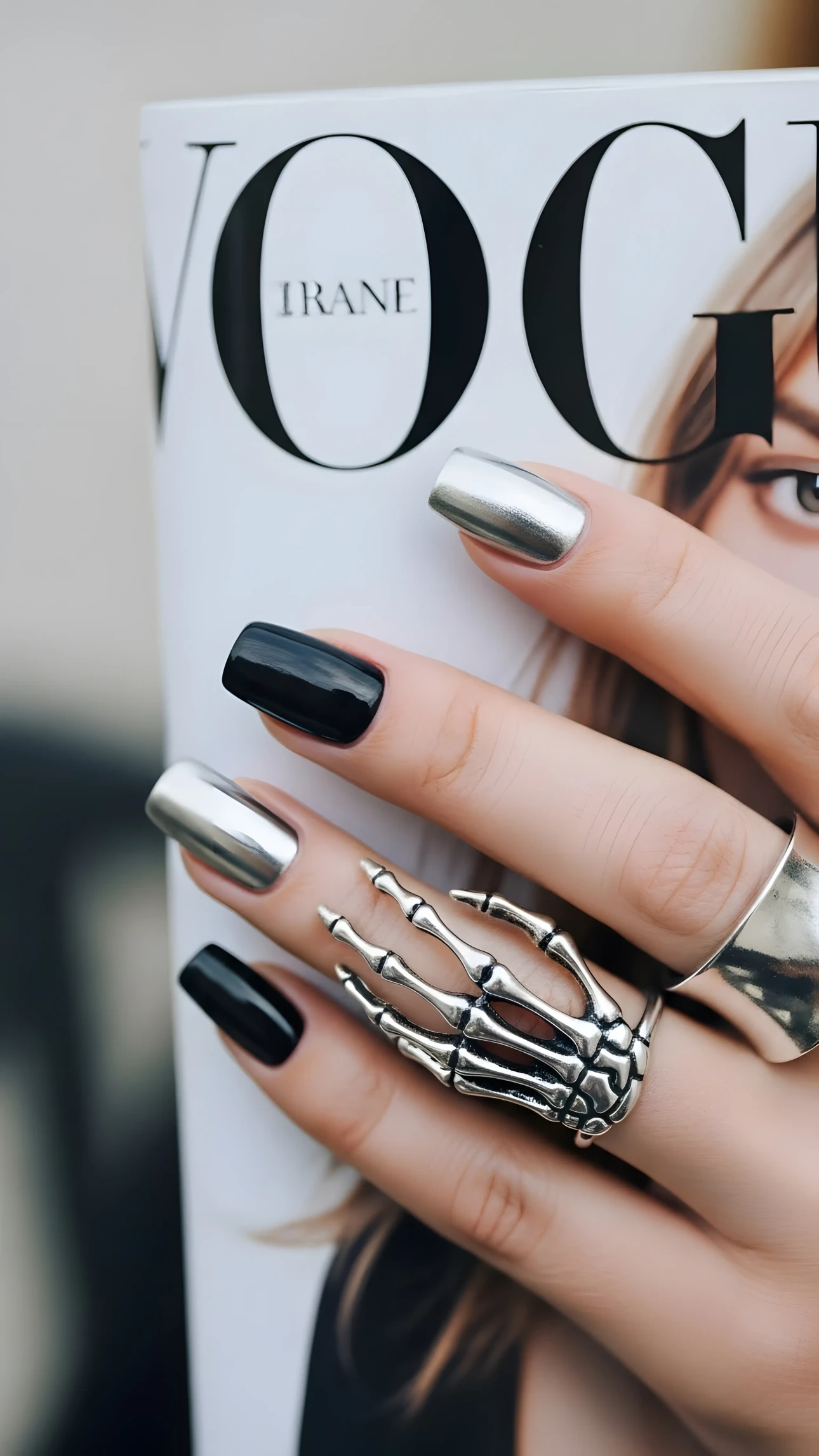 ernating black and silver metallic nail polish, creating a modern and edgy aesthetic. A prominent skeleton hand ring adds a gothic touch, making it perfect for fashion, beauty, or lifestyle projects that aim for a darker, more alternative vibe. The cool-toned color palette enhances the overall mood, while the juxtaposition of smooth, polished nails and the intricate details of the ring creates visual interest. The hand is posed against a blurred background, ensuring the focus remains on the manicure and jewelry.
