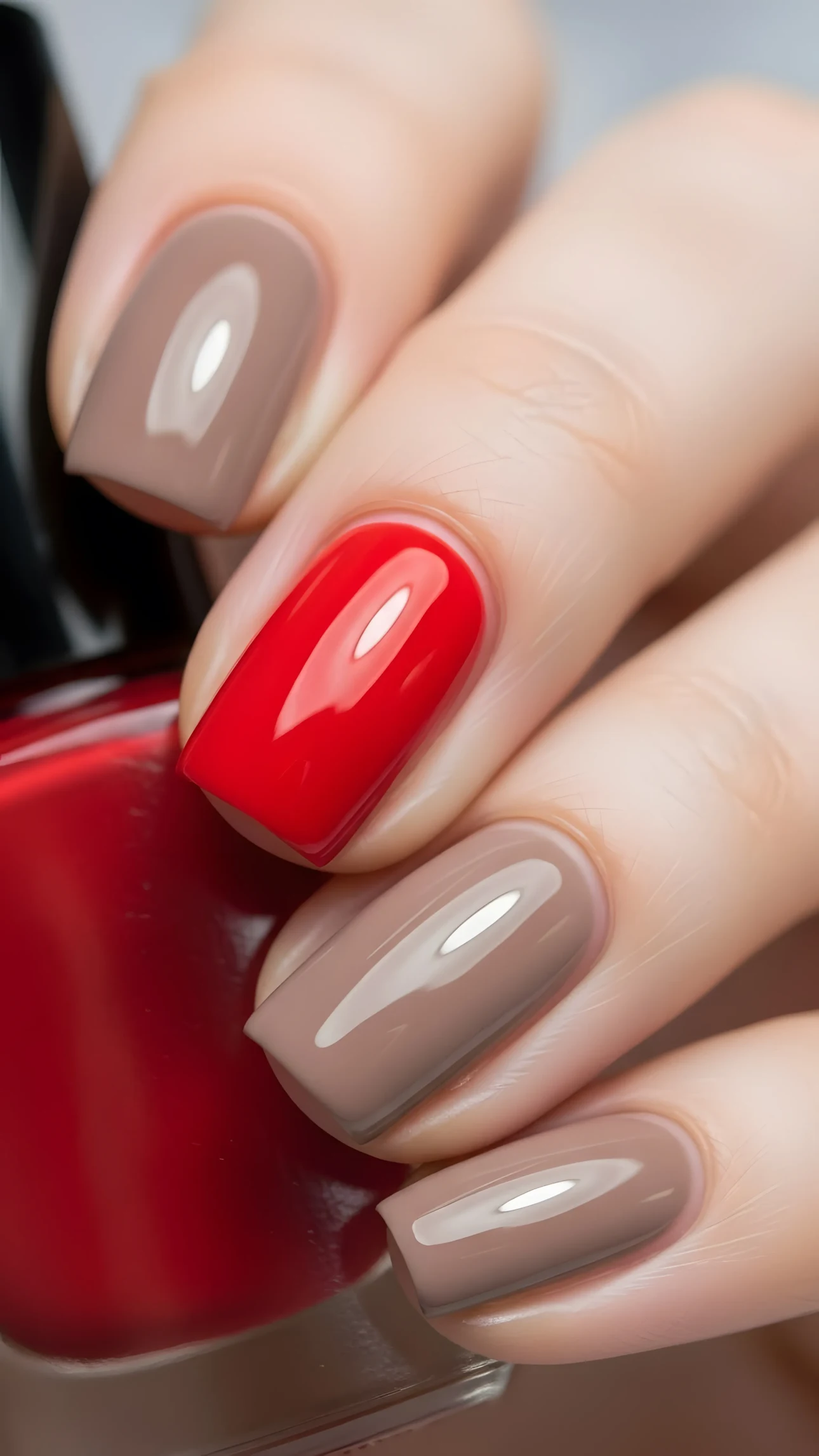 Close-up of a manicured hand with glossy red and taupe nail polish, showcasing a modern and stylish color combination.