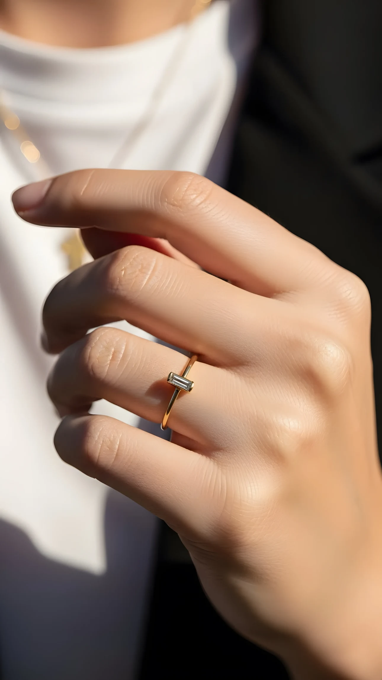Close-up of a woman's hand wearing a delicate gold ring with a baguette diamond, illuminated by warm sunlight.