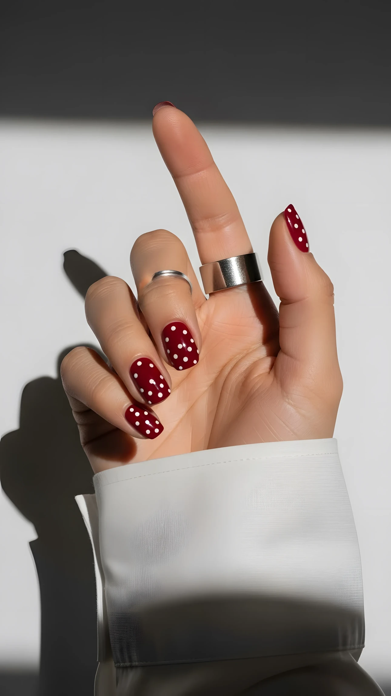 Hand with red polka dot nails and silver rings in bright studio lighting, showcasing a modern manicure and jewelry style.