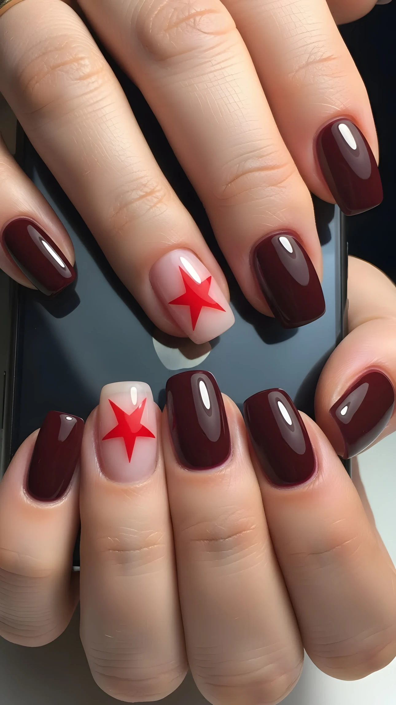 Close-up of hands with burgundy and red star nail art holding a smartphone, showcasing a stylish manicure.