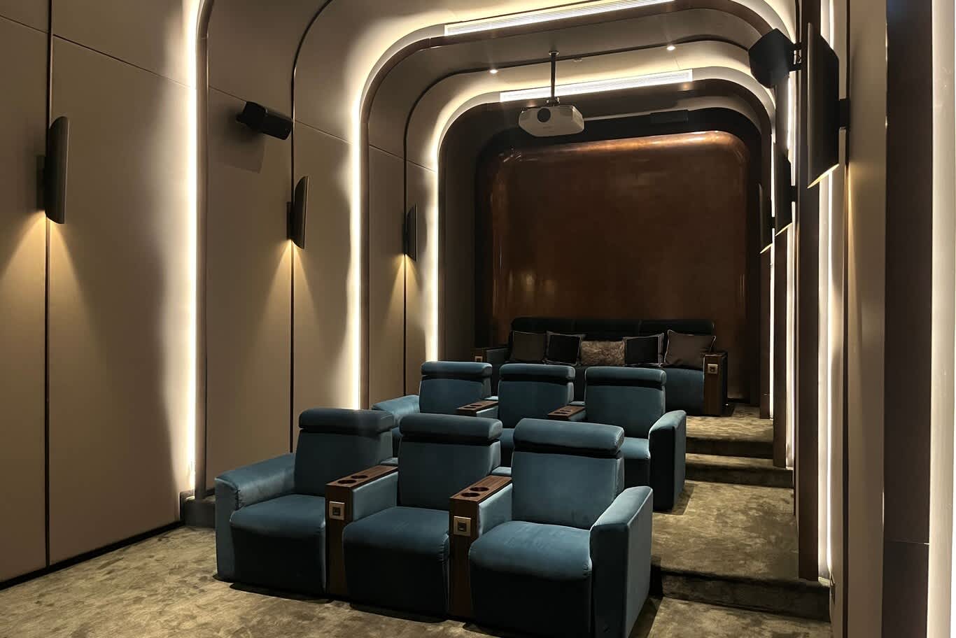•	Tiered home theater seating in teal velvet recliners beneath a vaulted ceiling with lit ribs