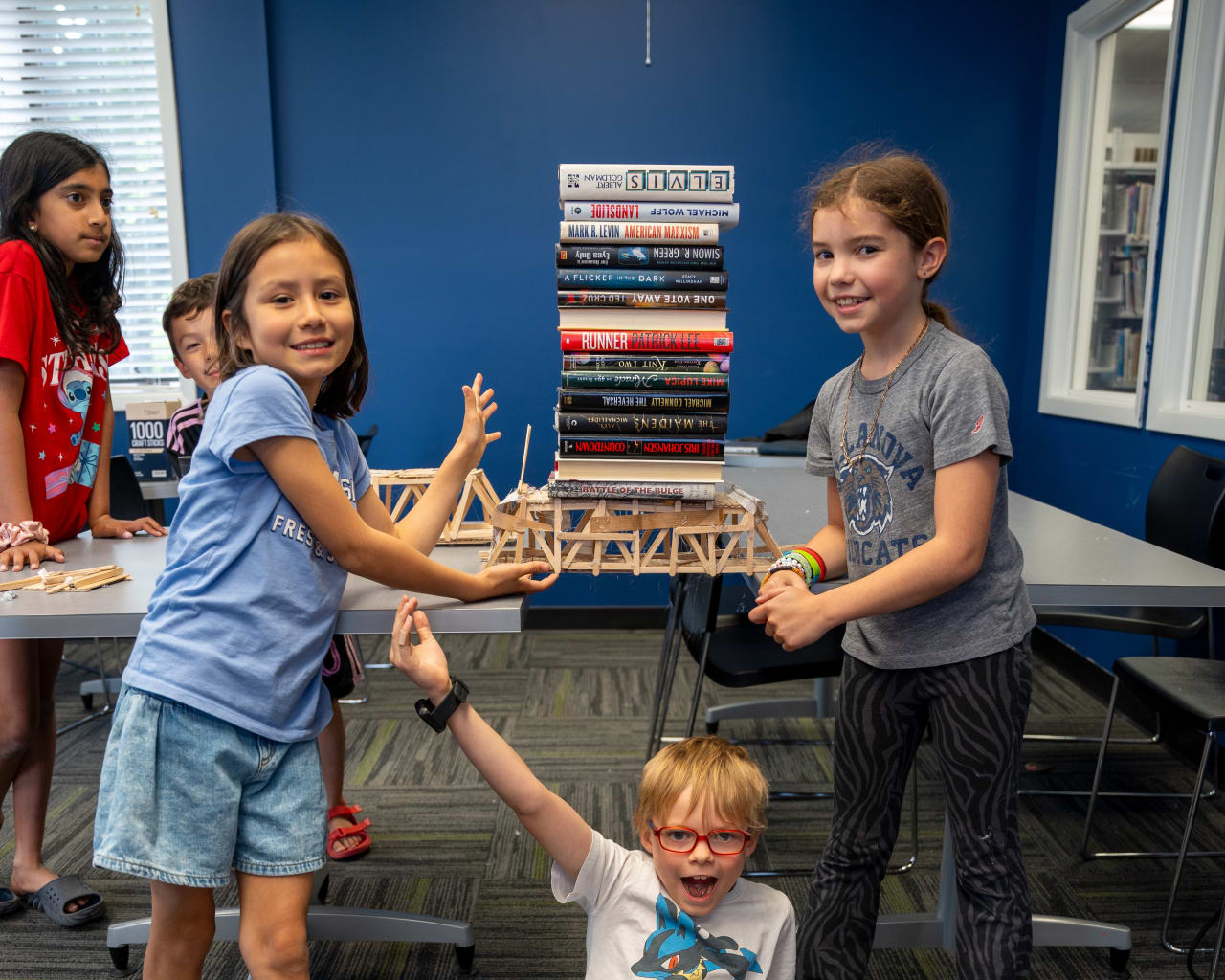 Young Hispanic youth collaborating on a popsicle stick engineering project at a workshop table (1/8)