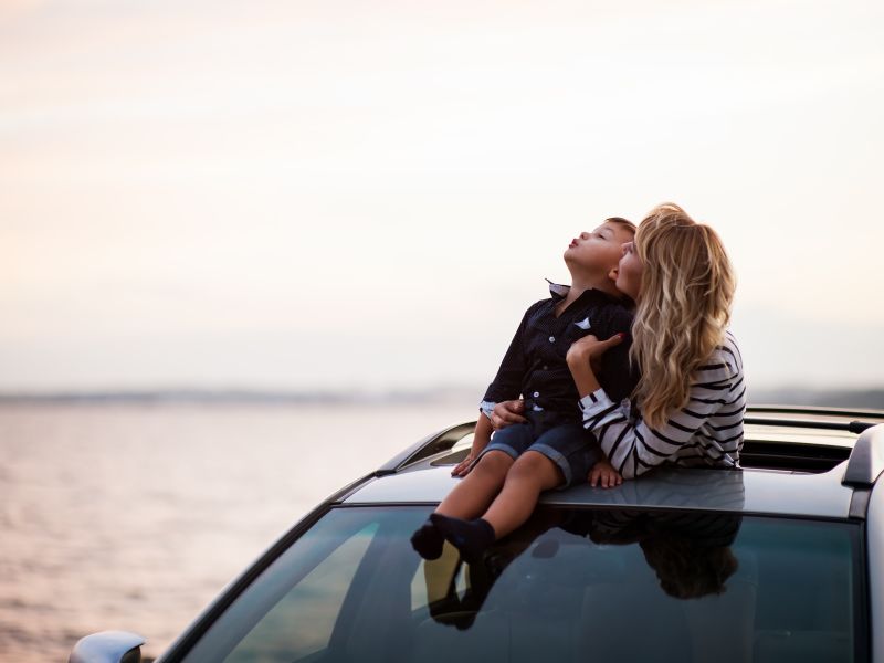 Mother and son looking out onto the ocean from a repaired automobile. Interest free car repair loans can be used in emergencies when you need a working car for work and transportation.
