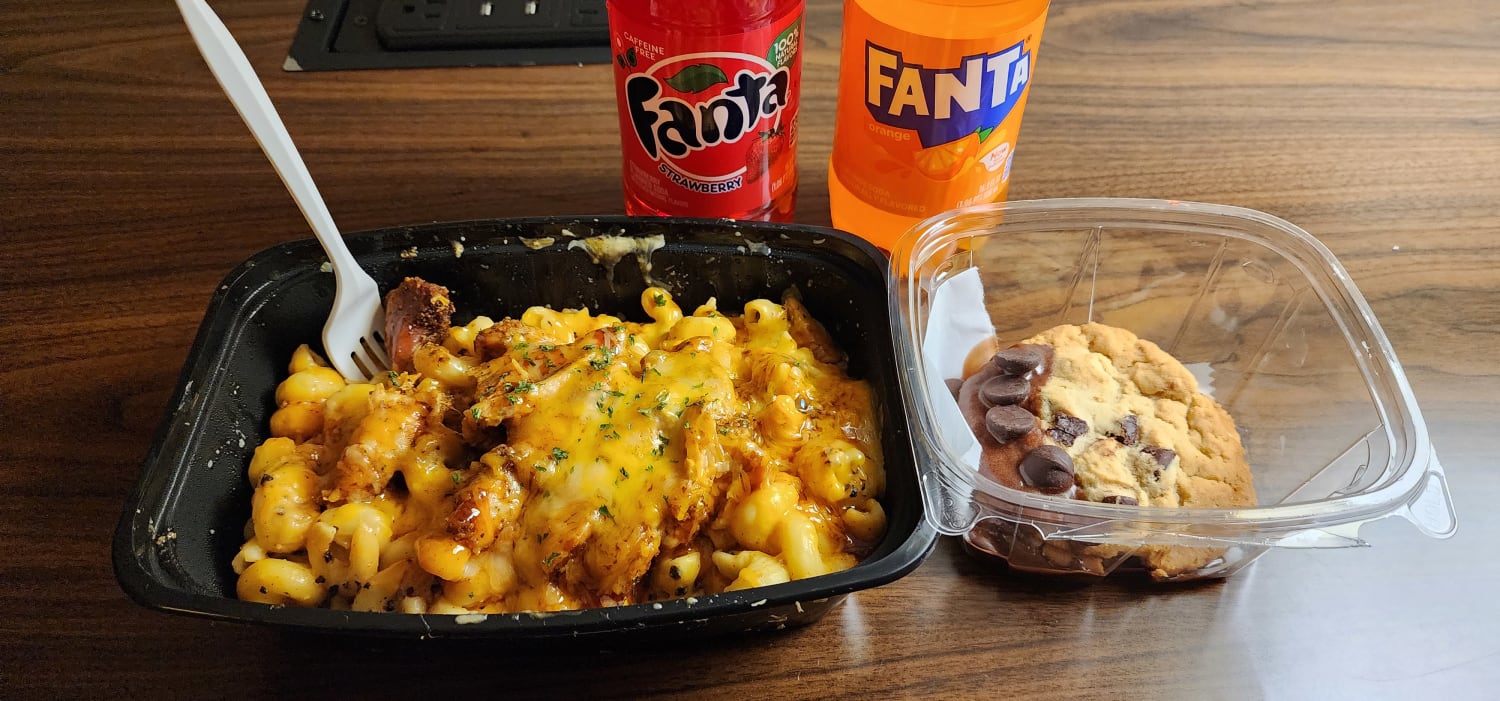a bowl of of chicken and macaroni and cheese with chocolate cookies in another container and two bottles of fanta, one strawberry, the other orange