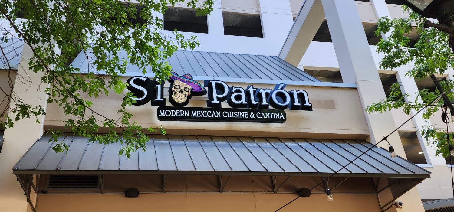 A sign for Si Patron Modern Mexican Cuisine and Cantina with a colorful skull wearing a sombrero.