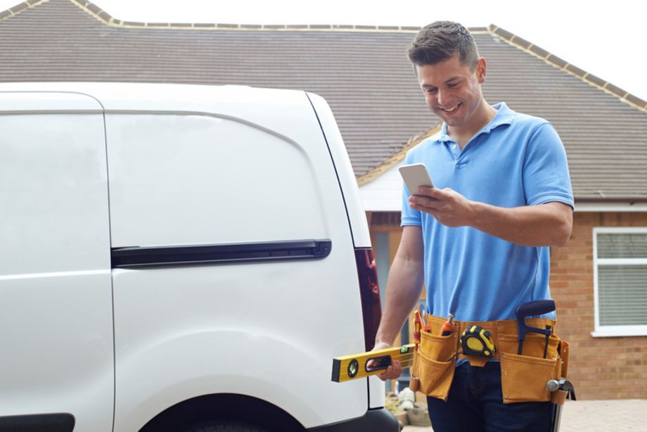 Sole trader builder outside a white van holding a smartphone