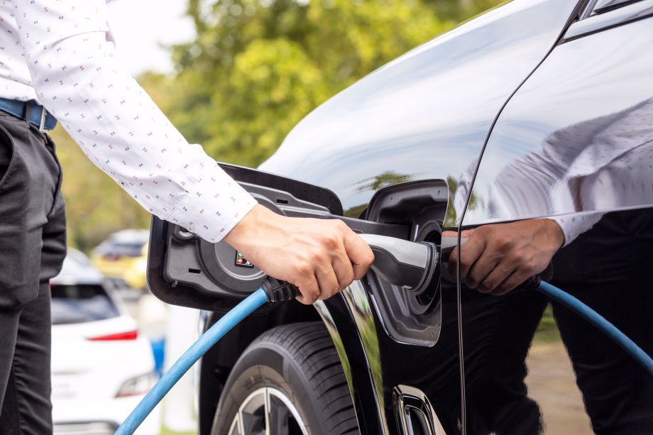 Man charging a black electric car at a charge point